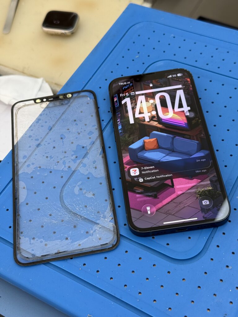 กระจกหน้าจอ iPhone ที่ถอดออกวางข้างเครื่องบนแผ่นรองซ่อม